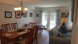 A dining area with a wooden table and chairs, a chandelier, and a sofa in the living area. - Beautifully decorated townhome just steps from the beach & Lighthouse (Tybee Island)