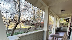 A covered porch with a table and chairs, a wooden bench, and a view of trees and a fence.