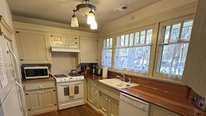 A kitchen with wooden flooring, white cabinets, a stove, microwave, sink, and a ceiling fan.