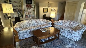 A living room with a sectional sofa, a coffee table, a rug, a bookshelf, and a dining area.