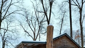 A log cabin with a porch and a covered deck, surrounded by snow and trees.