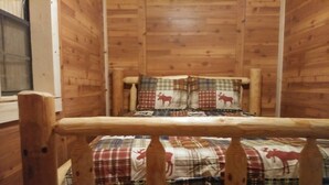 A wooden cabin room with a bed featuring plaid bedding with animal prints.