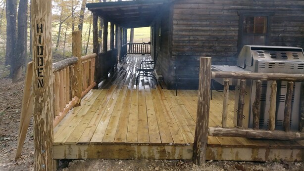A wooden cabin with a covered porch and a grill area.