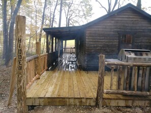 Een houten hut met een overdekte veranda en een barbecueplek.