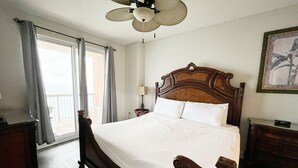 Un dormitorio con una cama grande, un ventilador de techo, una ventana con cortinas y un cuadro en la pared.