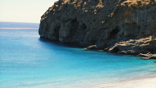 A beach with clear blue water, rocky cliffs, and several straw umbrellas on the sand. - Dreamy South Sea View Villa Residence with Pool - Garden Level (Sfakia)