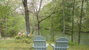 Twee Adirondack-stoelen gericht op een meer, omringd door bomen.
