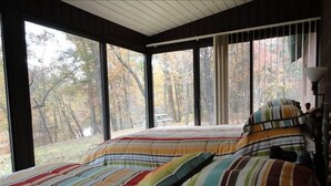 Een slaapkamer met een groot raam, een bed met gestreept beddengoed en uitzicht op bomen.