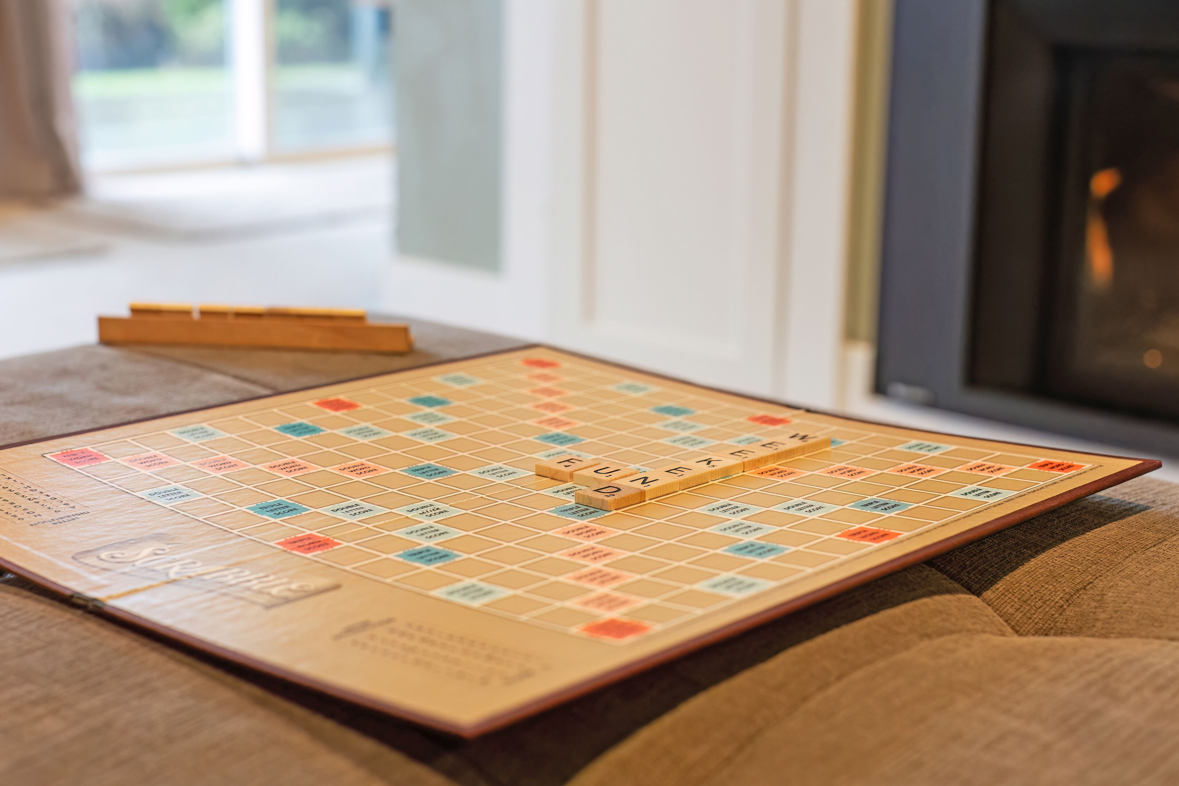 A Scrabble board game on a couch with wooden blocks spelling "FUN" in the center.