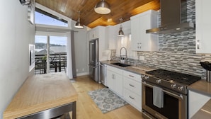 A modern kitchen with wooden ceiling beams, stainless steel appliances, and a view to the outside. - Pleasant Beach Getaway - Breathtaking Puget Sound Views and Steps from the Beach (Bainbridge Island)