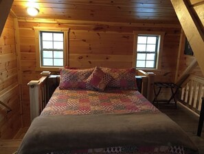 Cozy cabin with a sloped ceiling, featuring a bed and a small table with chair.