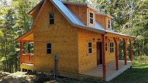 A wooden cabin with a porch, a small deck, and a metal roof. - "The Genoa" a Rustic Adventure - Amish-Built Deluxe Cabin  (Genoa)