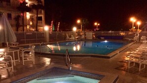 A swimming pool area with a hot tub, lounge chairs, and a poolside table.