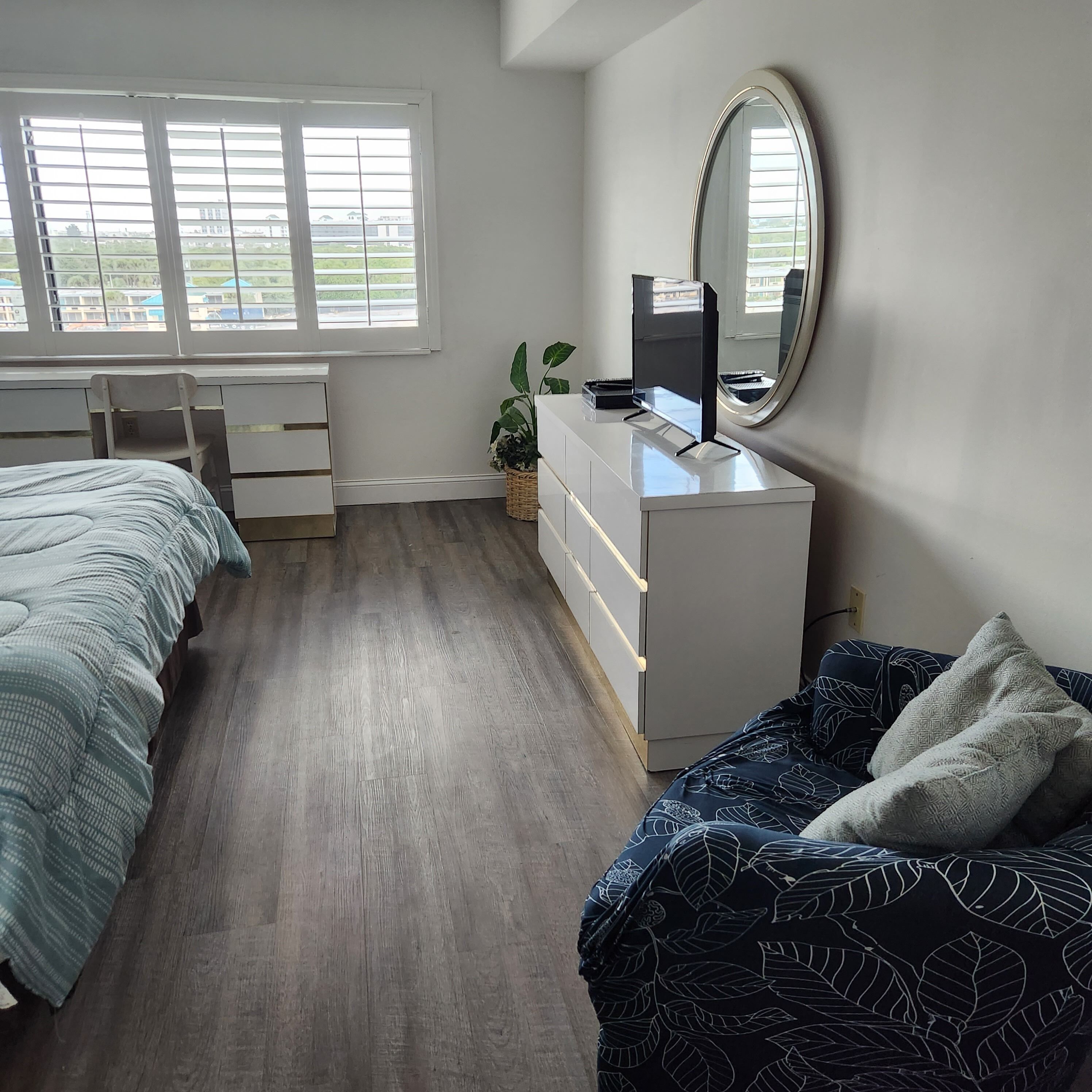 Quarto com cama, escrivaninha, cômoda, espelho e janela com persianas.