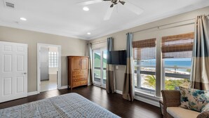 Une chambre avec un grand lit, un ventilateur de plafond, une télévision et une vue sur la plage.