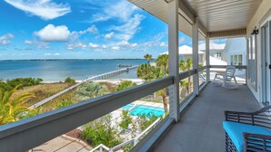 Un balcon abrité offrant une vue sur une plage, un quai et une piscine.