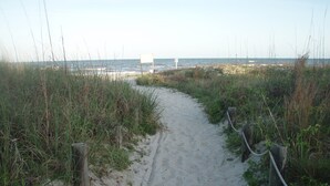 Un sentier de plage sablonneux, bordé de poteaux en bois et de cordes, qui mène à l’océan.