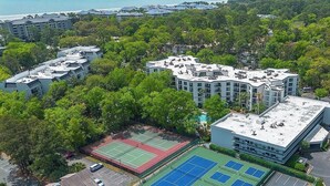 Vue aérienne d’un quartier résidentiel comprenant plusieurs immeubles, un court de tennis et un parking.