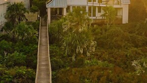 Une maison dotée d’une longue terrasse en bois qui y mène, entourée d’une végétation luxuriante.