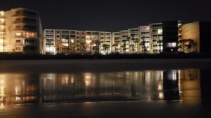 Un hotel amb façana al mar i diversos edificis que es reflecteixen en l'aigua tranquil·la.