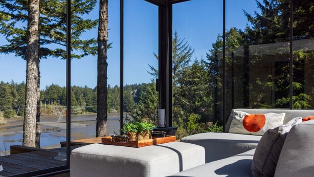 Una sala de estar moderna con un ventanal grande, un sofá y una mesa de madera con objetos decorativos.
