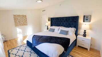 Un dormitorio con una cama grande, una mesita de noche, una lámpara de pared y un tapete estampado.