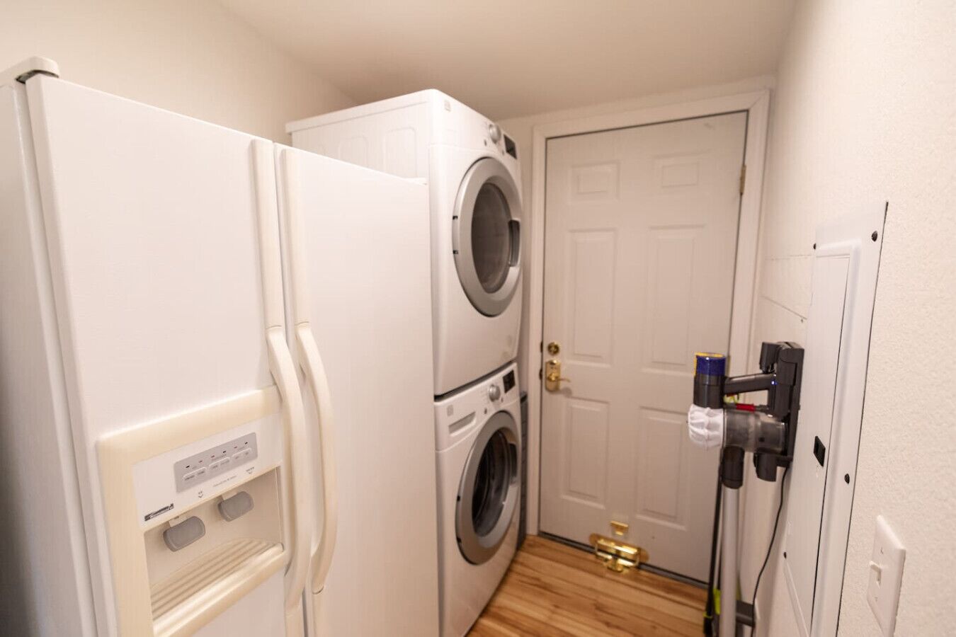 A laundry room with a washing machine and dryer, a refrigerator, and a door with a lock and a towel hanging on the handle.