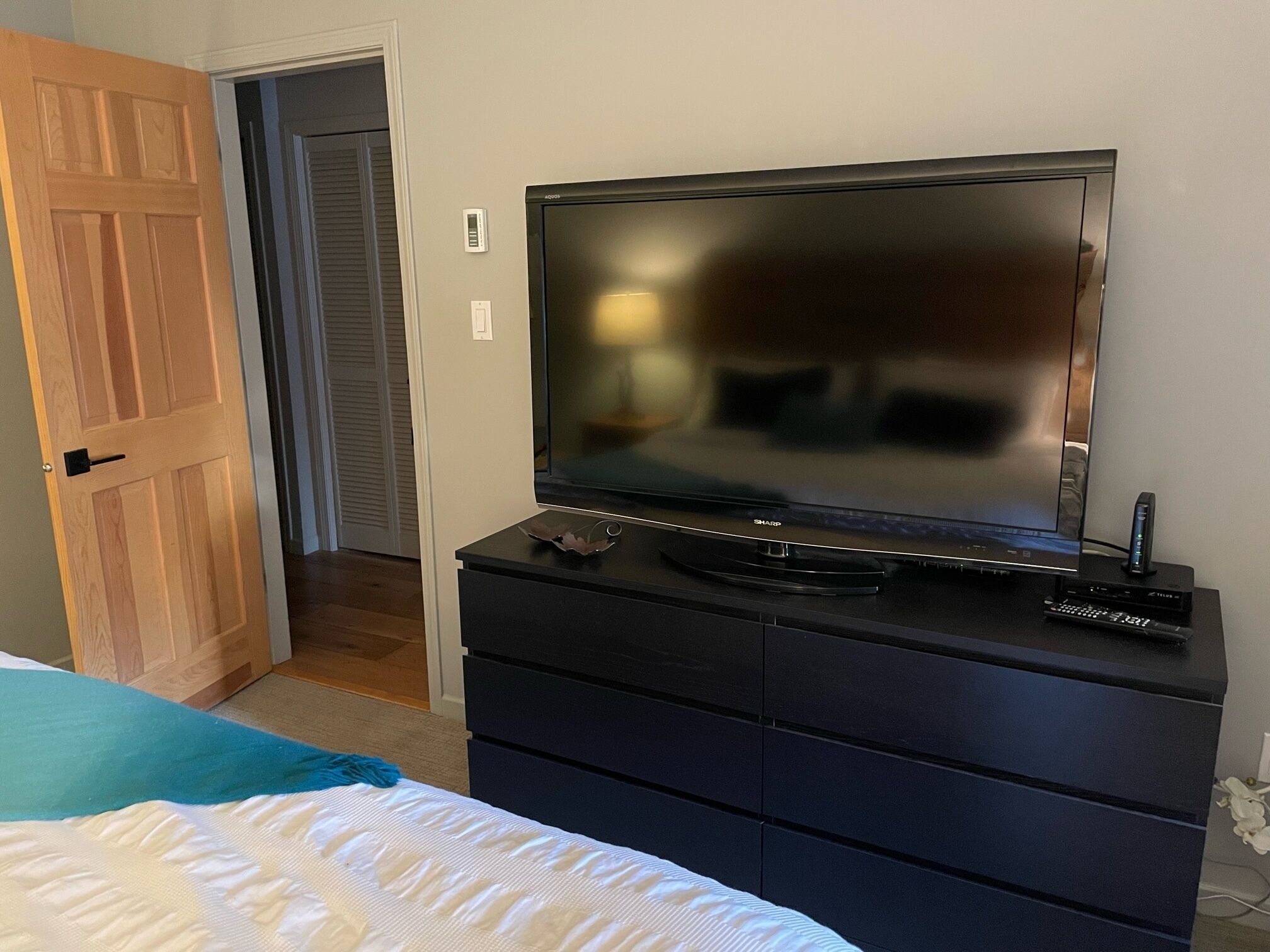 Une chambre avec une télévision posée sur une commode, un lit recouvert d’une couette bleue et blanche, et une porte en bois.