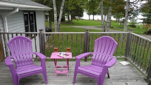 Un pontile in legno con due poltrone Adirondack viola e un piccolo tavolino rosa con bevande e un libro.