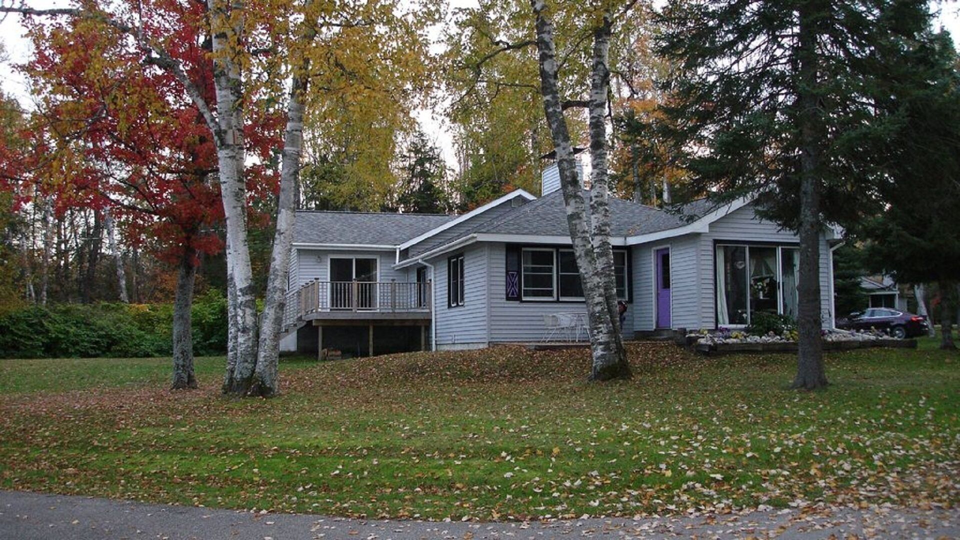 A single-story house with a front deck, surrounded by trees with autumn foliage.