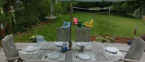Una terraza de madera con una mesa dispuesta para comer, rodeada de sillas y una sombrilla que da sombra.