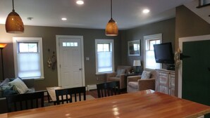 A spacious living room with a wooden dining table, two armchairs, a sofa, and a television. - Quaint,,,Quiet..up island feel yet a short walk to town and harbor (Oak Bluffs)