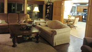 A living room with a sofa, a coffee table, and a lamp. There is a door leading to a kitchen.