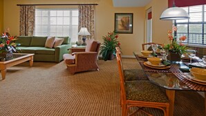 A living room with a green sofa, wicker armchair, and dining table set for a meal. - Ultimate Orlando Adventure: Orange Lake Resort - Disney, Universal, Sea World! (Kissimmee)