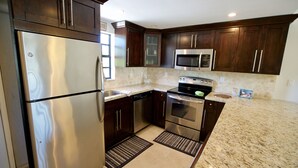 A modern kitchen with stainless steel appliances, dark wood cabinets, and a granite countertop. - Updated Key Largo Townhome • Pool • Saltwater Lagoon • Beach • Oceanfront Access (Key Largo)
