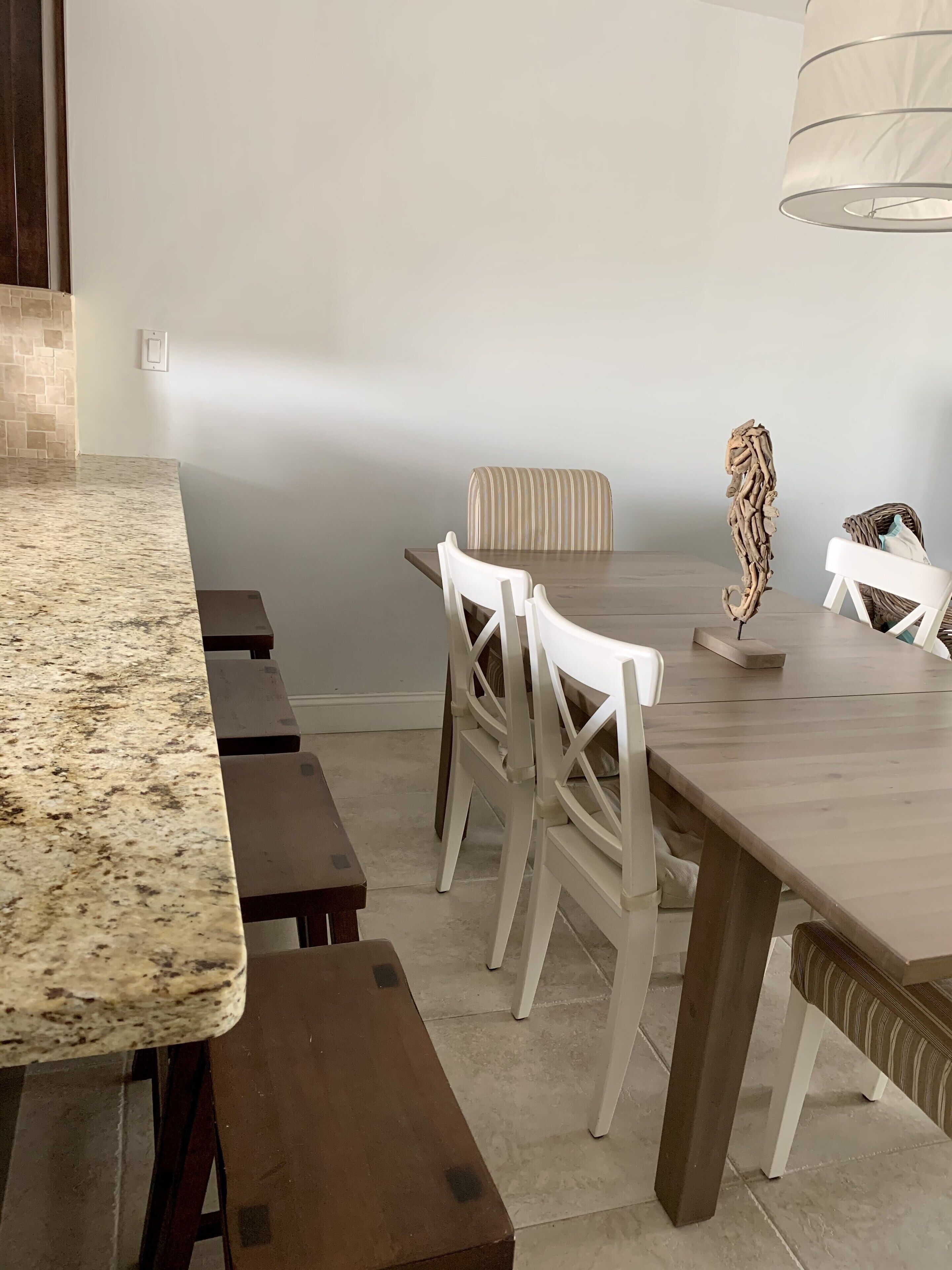 A dining area with a marble countertop, wooden benches, and white chairs.