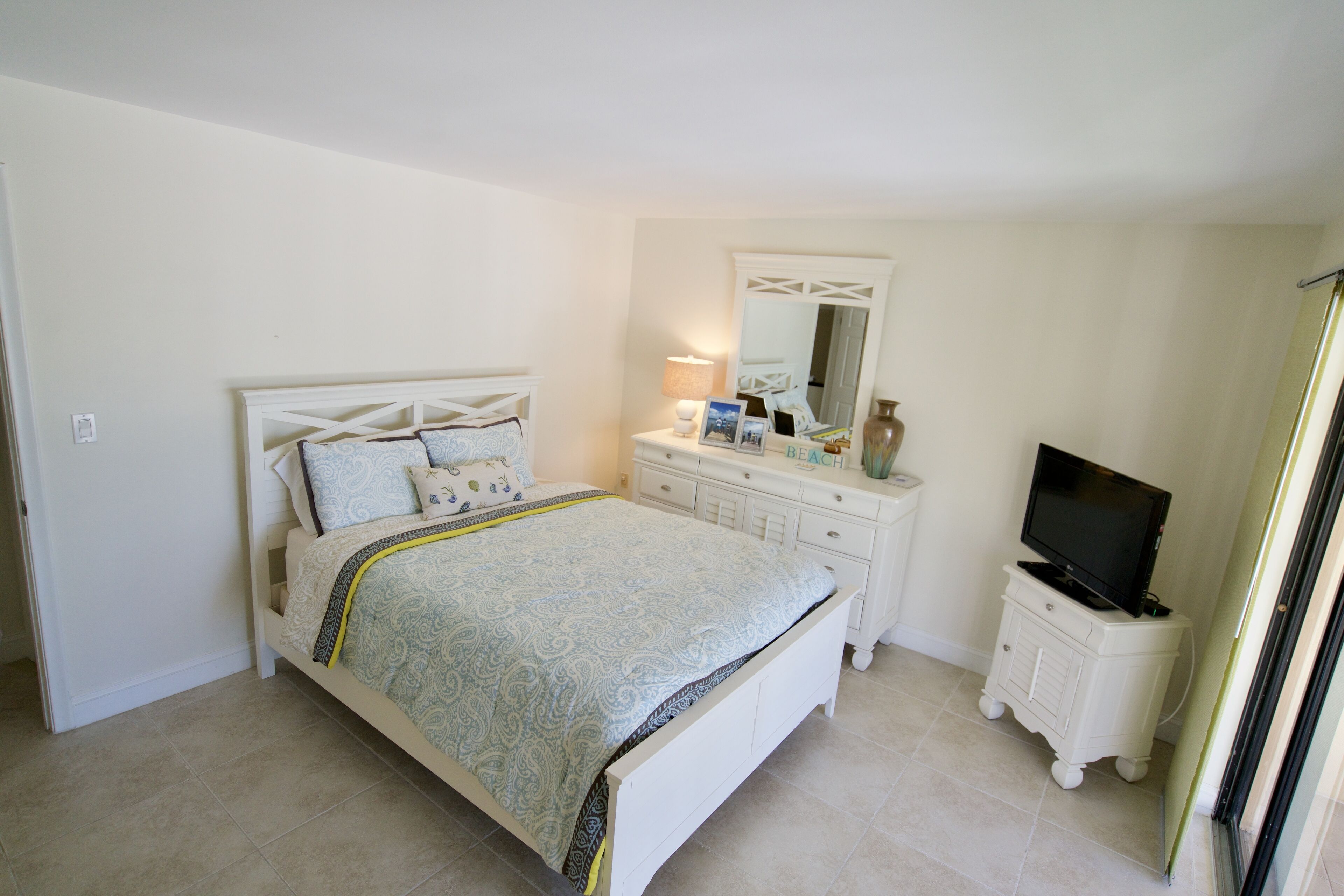 Un dormitorio con cama, cómoda, televisor y espejo.