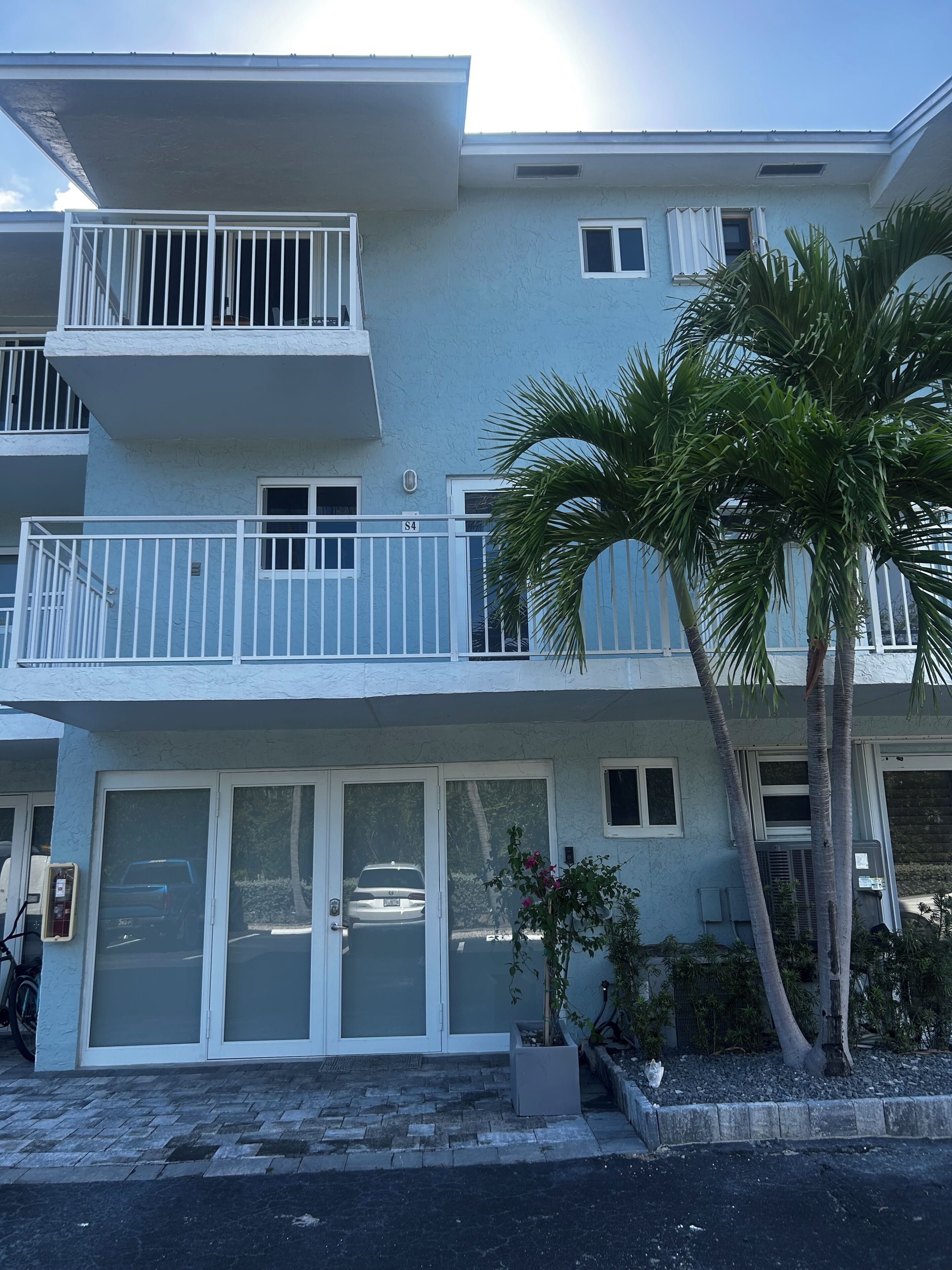 A multi-story building with balconies, a gated entrance, and a palm tree.