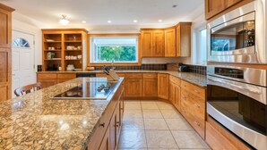 Een moderne keuken met granieten aanrechtbladen, houten keukenkastjes, roestvrijstalen apparatuur en een groot raam dat voor natuurlijk licht zorgt.
