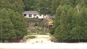 Ett hus med en brygga som sträcker sig ut i en sjö, omgivet av tät skog.