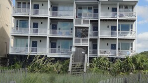 Un immeuble résidentiel à plusieurs étages, doté de balcons, d’une clôture en bois et entouré de végétation.