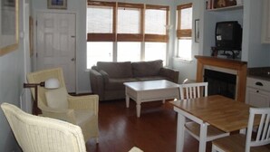 Un salon comprenant un canapé, une table basse, une table à manger avec des chaises, un téléviseur et une cheminée.