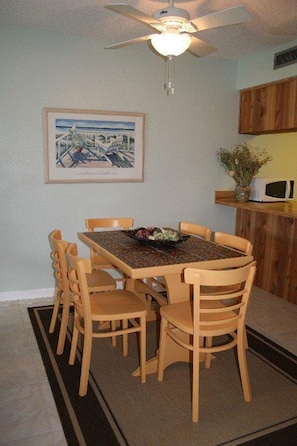 Een eethoek met een tafel en stoelen, een plafondventilator, een inlijsting foto aan de muur en een magnetron op een aanrecht.
