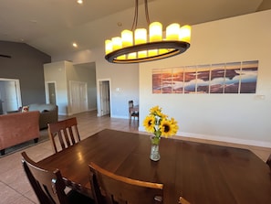 A dining area with a large wooden table, chairs, a vase with sunflowers, and a wall-mounted painting.