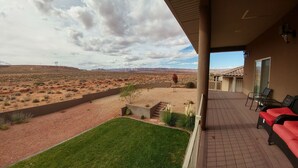 Un patio con vistas a un paisaje desértico, una zona ajardinada y un edificio con techo de tejas.