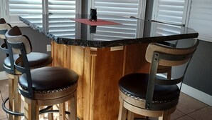 Una cocina con isla central, sillas de madera y persianas blancas en las ventanas.