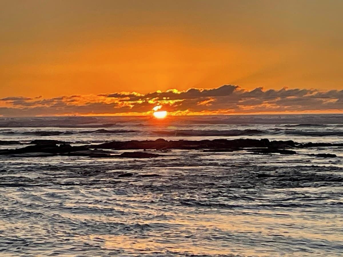A sunset over the ocean with waves and a clear sky.