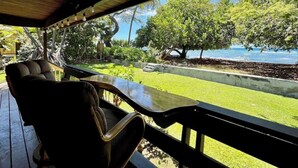 Un espace extérieur abrité, aménagé avec des sièges, offrant une vue sur l’océan et une végétation luxuriante.