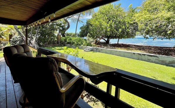 A covered outdoor seating area with a view of the ocean and lush greenery.