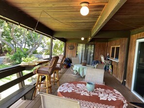 A covered outdoor seating area with wooden furniture and a table with a floral tablecloth.
